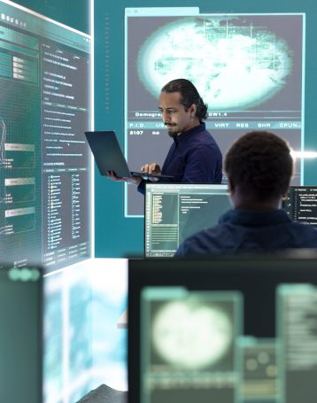 Professional hacker using ransomware and phishing tactics to compromise networks and gather intelligence for national security during cyberwarfare. Governmental spyware on big screen.