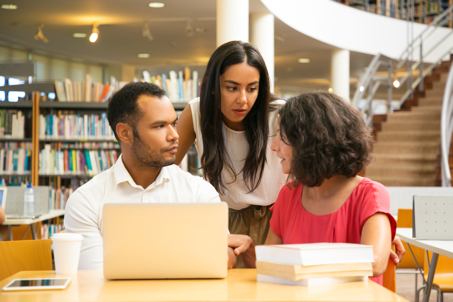 Serious students sitting at table in library with laptop